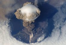volcanic ash cloud rising above an island