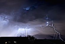 Bright lightning forks through dark storm clouds across a dramatic night sky.